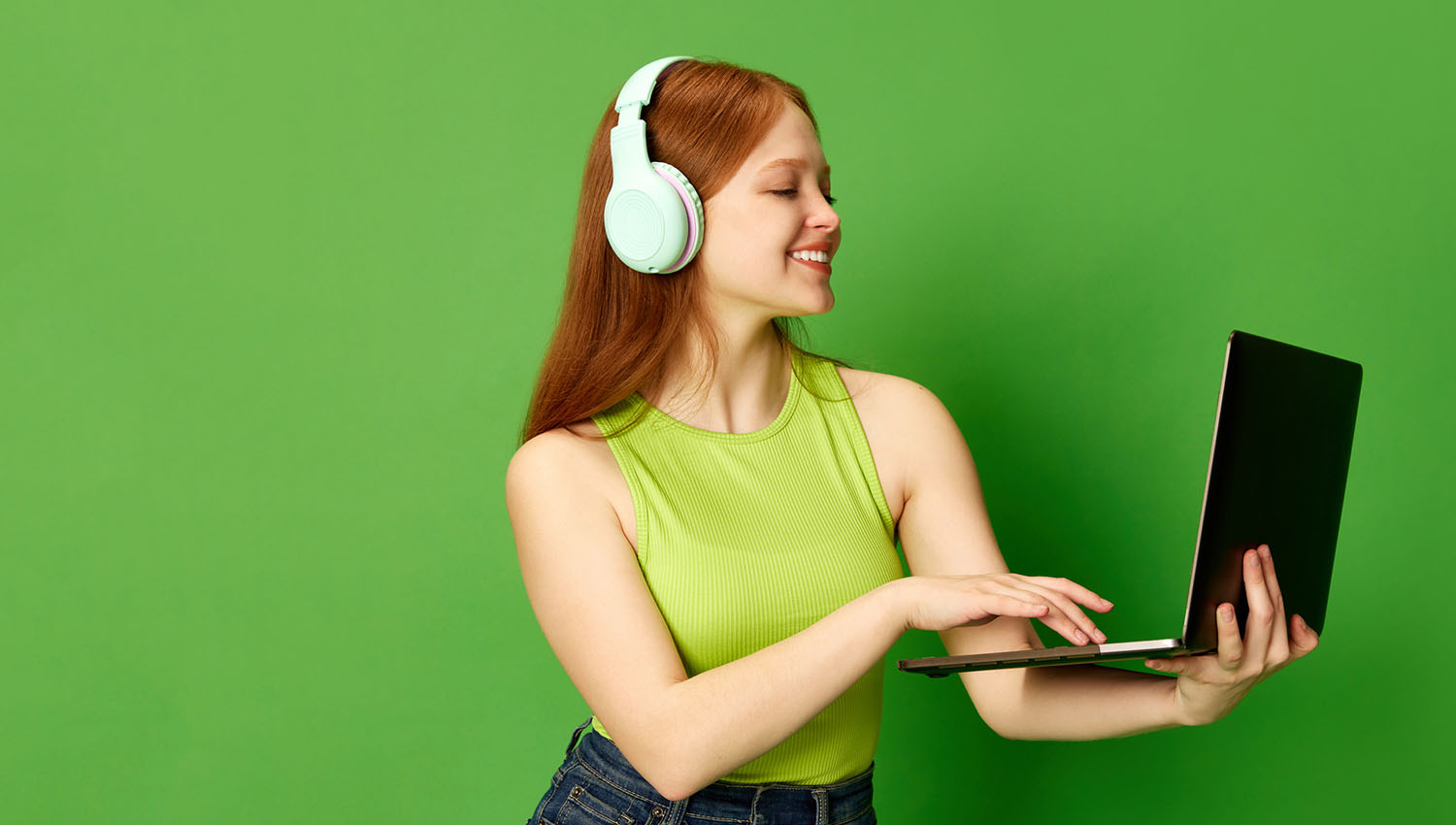 Young woman in a green top using a laptop while wearing matching headphones