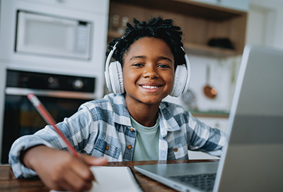 Smiling student wearing headphones, studying with a laptop and notebook at home.