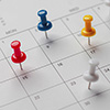 Close-up of a calendar with colorful push pins marking important dates and deadlines.