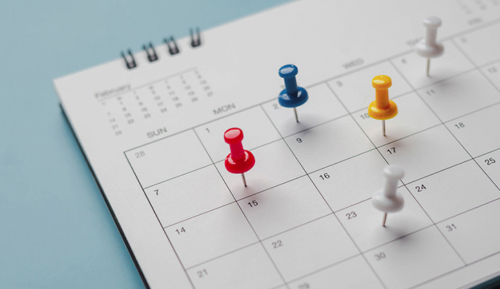 Close-up of a calendar with colorful push pins marking important dates and deadlines.