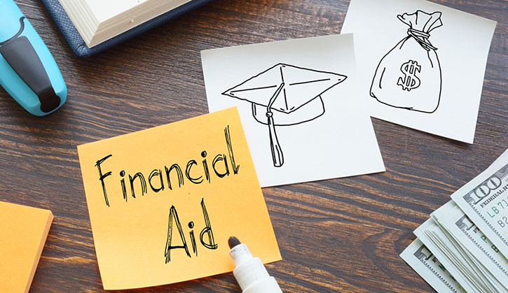 Financial aid concept with sticky note, graduation cap sketch, money bag drawing, and cash on a wooden desk.